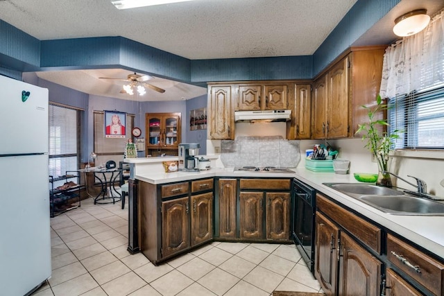 kitchen featuring freestanding refrigerator, a peninsula, light countertops, under cabinet range hood, and a sink