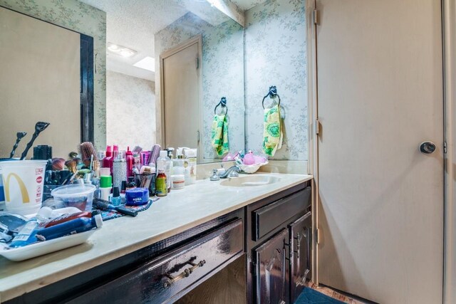full bath with vanity, wallpapered walls, and a textured ceiling