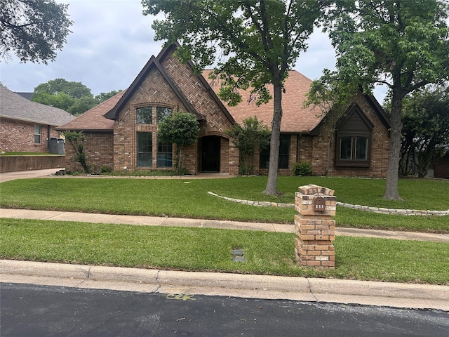 tudor house with brick siding, a front yard, and roof with shingles