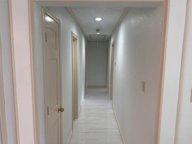 hall featuring crown molding, baseboards, a textured wall, and attic access