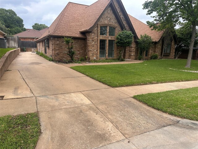tudor house featuring brick siding, fence, a shingled roof, and a front yard