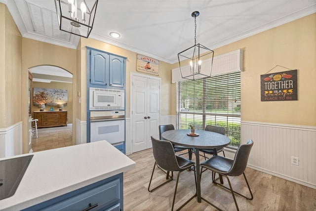 dining space with crown molding, a wainscoted wall, light wood-style flooring, and a chandelier