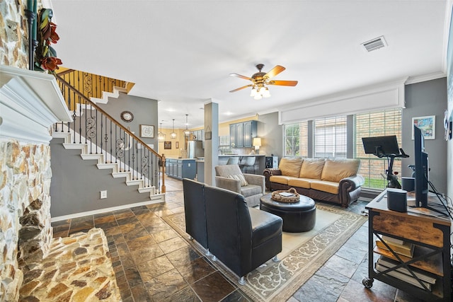 living room featuring visible vents, stone tile floors, crown molding, ceiling fan, and stairway