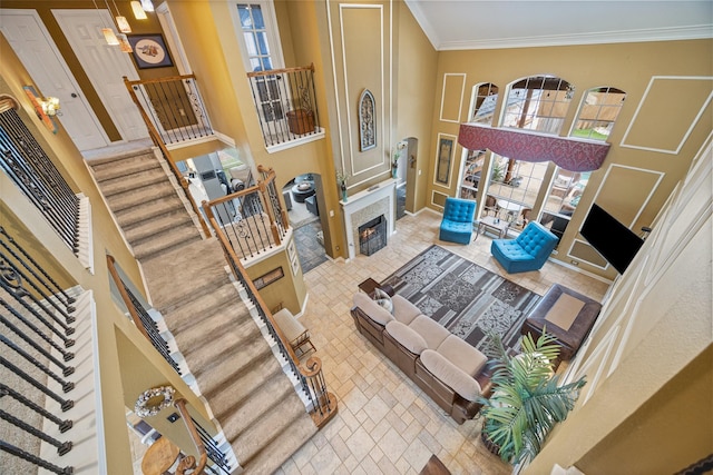 living area featuring stairs, crown molding, a fireplace with flush hearth, and a high ceiling
