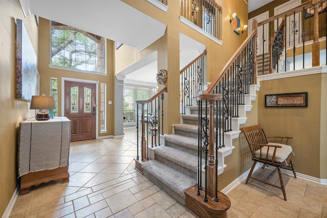 foyer featuring baseboards, stone tile floors, stairs, and a towering ceiling