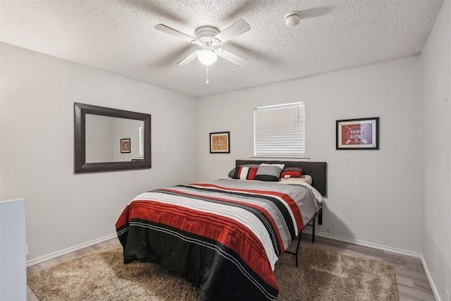 bedroom featuring baseboards, ceiling fan, a textured ceiling, and wood finished floors