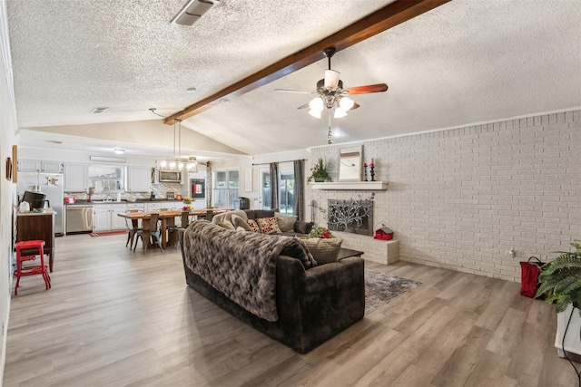 living room featuring brick wall, light wood-style floors, ceiling fan, vaulted ceiling with beams, and a textured ceiling