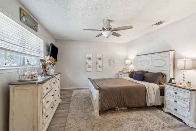 bedroom featuring light wood-style floors, a textured ceiling, a ceiling fan, baseboards, and visible vents