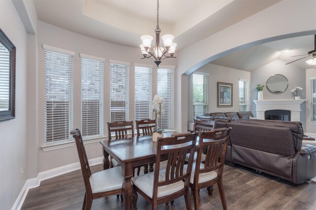 dining area with a glass covered fireplace, baseboards, dark wood-type flooring, arched walkways, and ceiling fan with notable chandelier