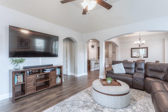 living area featuring baseboards, ceiling fan with notable chandelier, dark wood-style flooring, and arched walkways