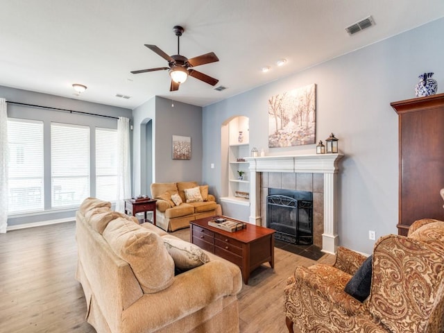 living area featuring visible vents, light wood-style floors, ceiling fan, a tile fireplace, and arched walkways