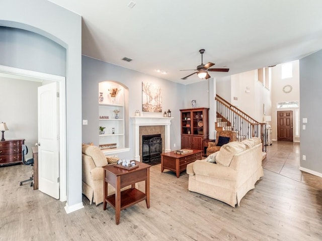 living area with a tiled fireplace, stairs, ceiling fan, and light wood-type flooring