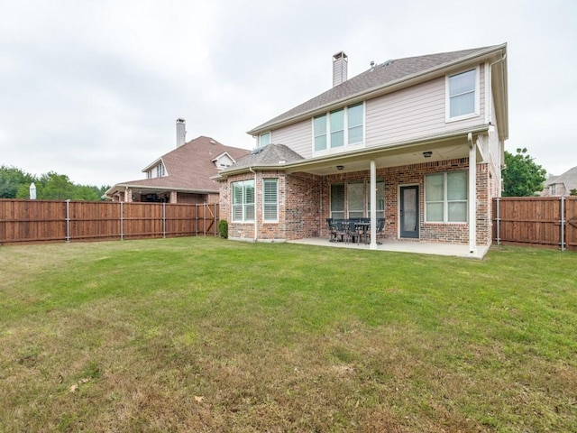 rear view of house with a chimney, a lawn, brick siding, a fenced backyard, and a patio