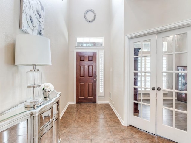 entryway with french doors, light tile patterned flooring, a high ceiling, and baseboards