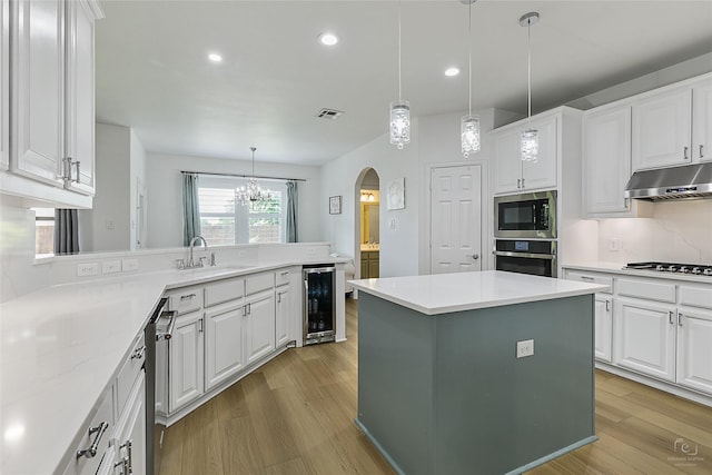 kitchen with a sink, under cabinet range hood, wine cooler, stainless steel appliances, and arched walkways