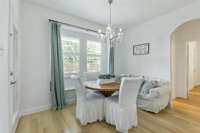 dining space with arched walkways, a chandelier, light wood-type flooring, and baseboards