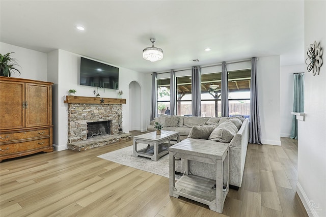 living area featuring arched walkways, baseboards, a stone fireplace, light wood-type flooring, and recessed lighting
