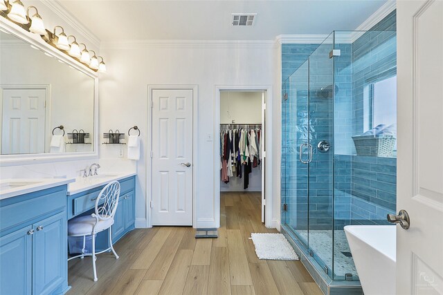 full bath with a stall shower, wood finished floors, double vanity, ornamental molding, and a soaking tub