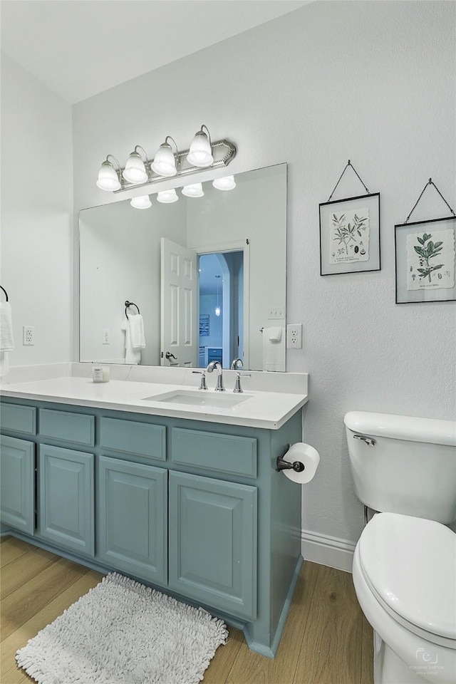 bathroom with wood finished floors, toilet, double vanity, and baseboards