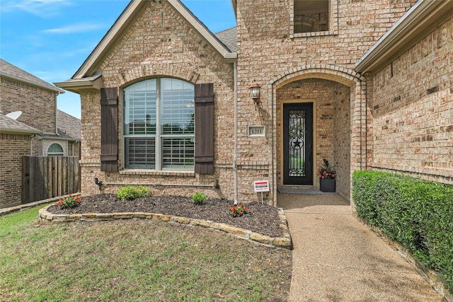 view of exterior entry featuring brick siding and fence
