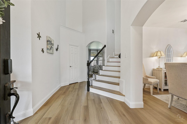 entrance foyer with arched walkways, light wood-style floors, baseboards, and stairs