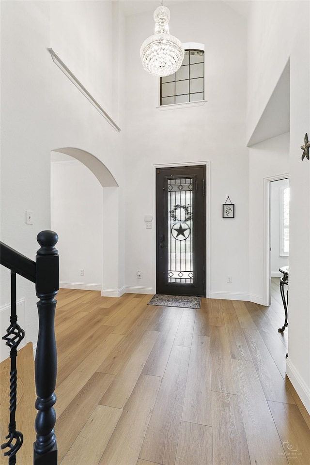 foyer with a chandelier, wood finished floors, arched walkways, baseboards, and a towering ceiling