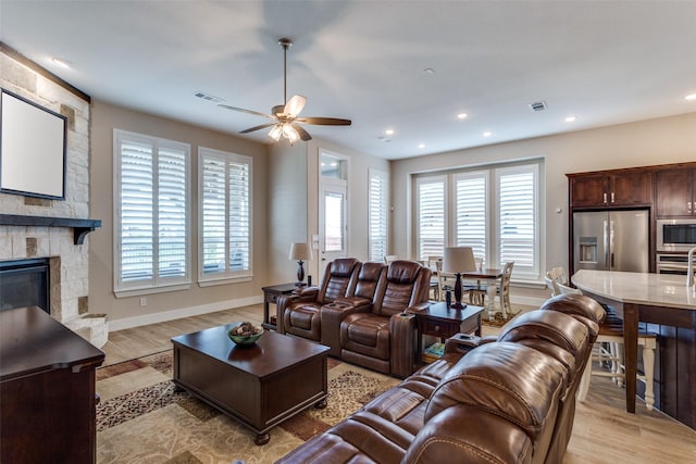 living room featuring visible vents, a fireplace, light wood-style floors, baseboards, and a ceiling fan