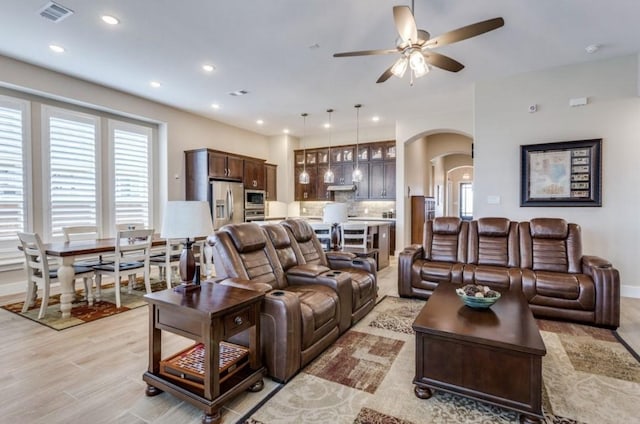 living room with a ceiling fan, visible vents, arched walkways, light wood finished floors, and recessed lighting