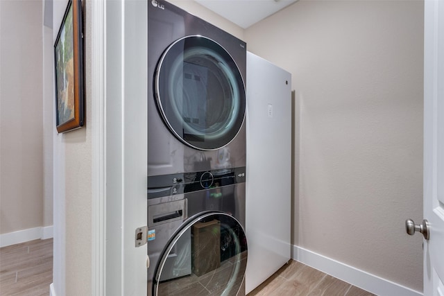 laundry room featuring baseboards, laundry area, stacked washer and dryer, and wood finished floors