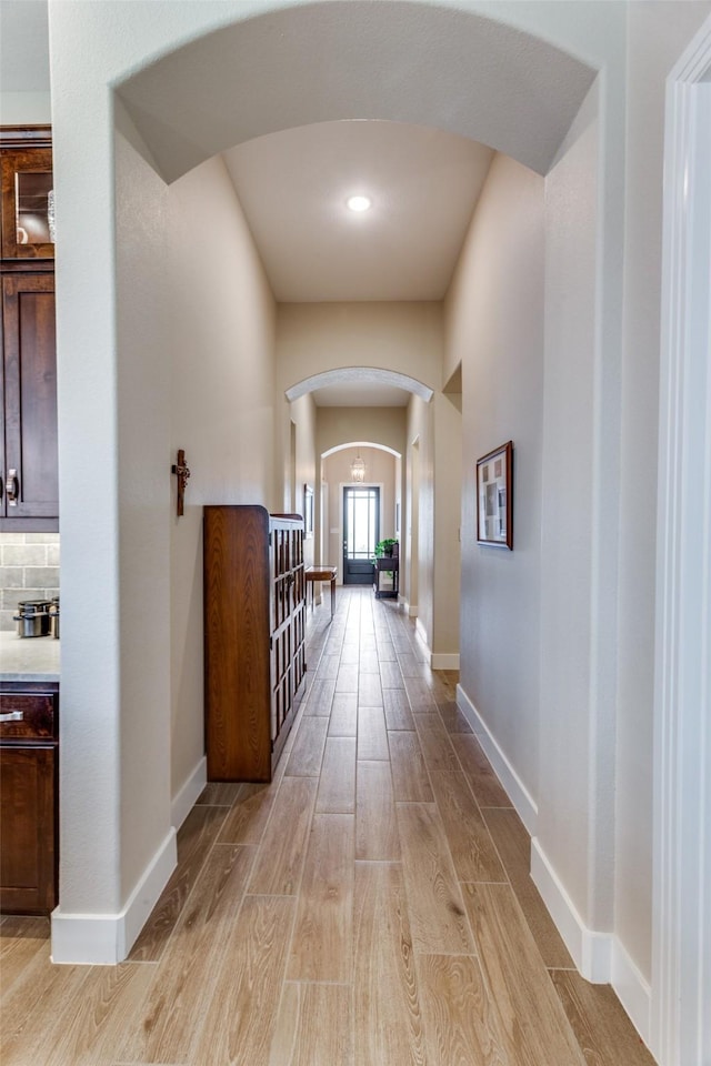 hallway with arched walkways, baseboards, and light wood-style flooring