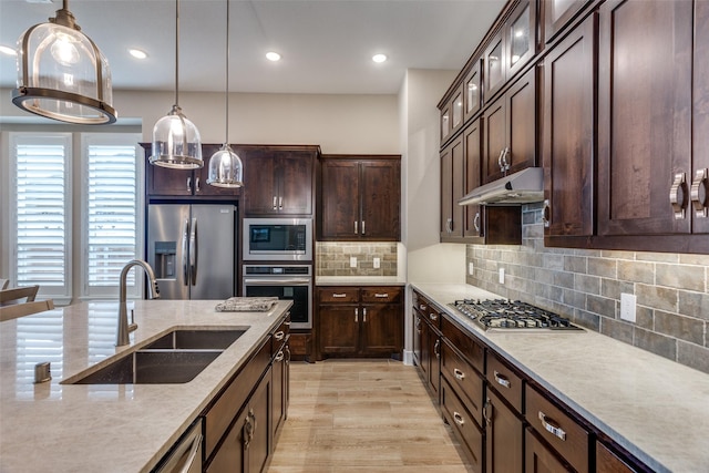 kitchen with dark brown cabinetry, appliances with stainless steel finishes, a sink, under cabinet range hood, and pendant lighting