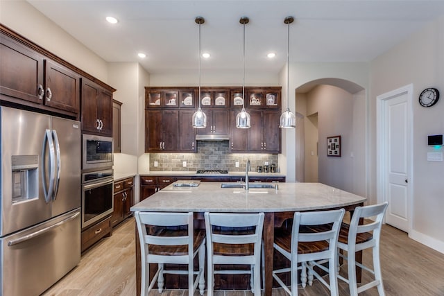 kitchen with dark brown cabinets, a sink, light wood finished floors, arched walkways, and stainless steel appliances