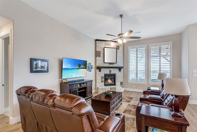 living room featuring ceiling fan, a fireplace, light wood-style floors, baseboards, and visible vents