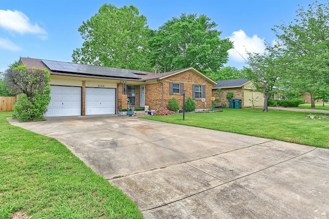 single story home featuring solar panels, a front yard, brick siding, concrete driveway, and an attached garage