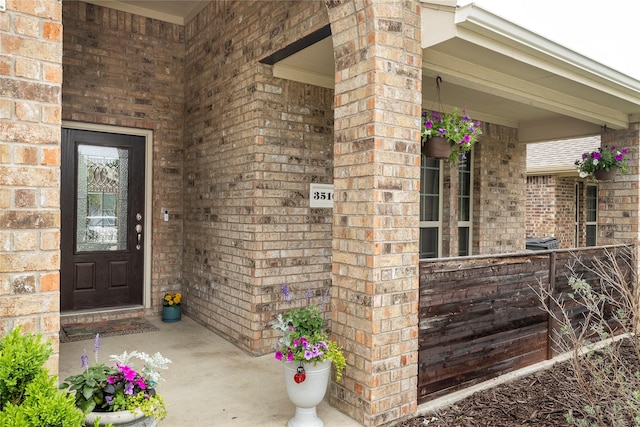 entrance to property with a porch and brick siding