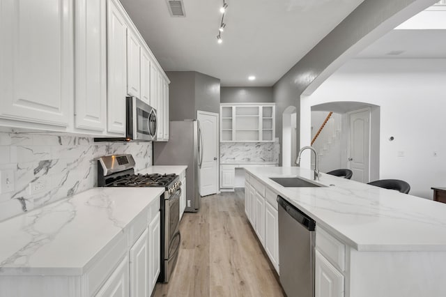 kitchen with arched walkways, open shelves, a sink, stainless steel appliances, and white cabinetry