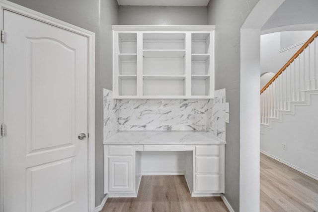 interior space with built in study area, arched walkways, and light wood finished floors