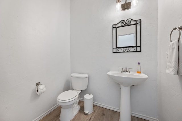 half bath with toilet, baseboards, a sink, and wood finished floors