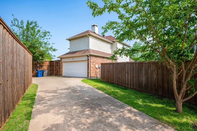 view of side of property with a chimney, a garage, brick siding, fence, and concrete driveway