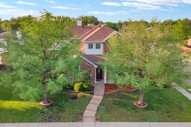 view of front of home with brick siding, a chimney, and a front yard