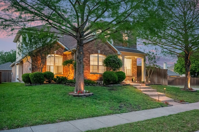 view of front facade with fence, a lawn, and brick siding