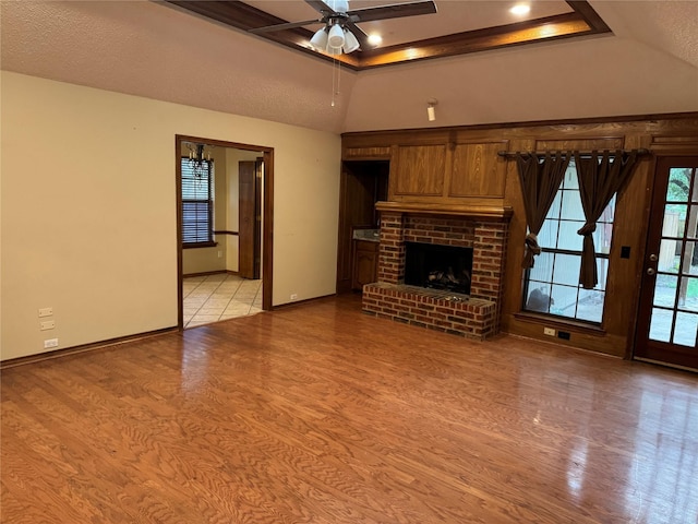 unfurnished living room featuring ceiling fan, a fireplace, baseboards, light wood-type flooring, and a tray ceiling