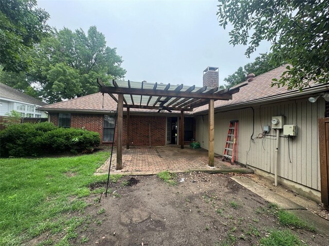 rear view of property featuring roof with shingles, a pergola, a chimney, a lawn, and a patio