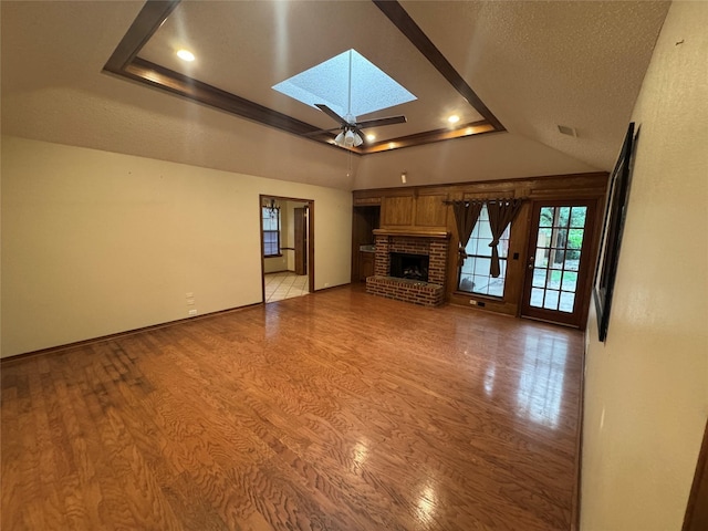 unfurnished living room with a raised ceiling, light wood finished floors, a brick fireplace, a skylight, and visible vents