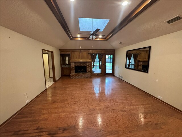 unfurnished living room with visible vents, light wood finished floors, lofted ceiling with skylight, and a fireplace