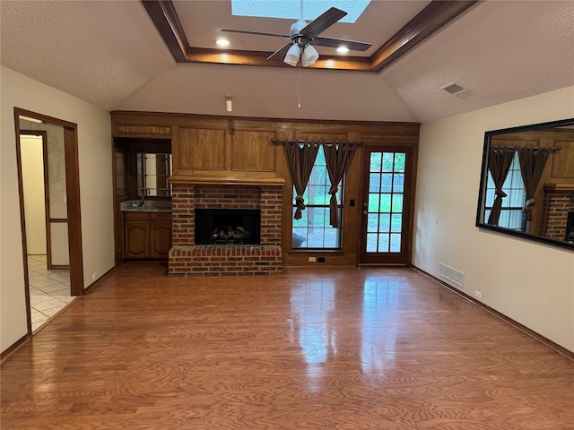 unfurnished living room with vaulted ceiling with skylight, a ceiling fan, visible vents, a brick fireplace, and light wood-type flooring