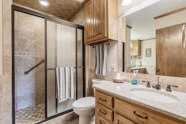 bathroom with crown molding, vanity, toilet, tile walls, and a stall shower