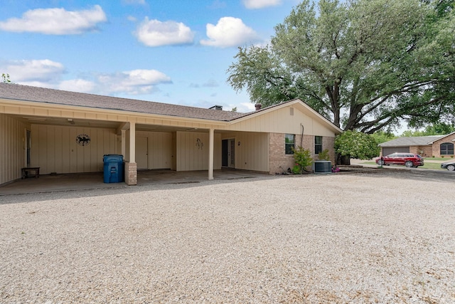 view of front of home with central air condition unit, brick siding, a carport, and gravel driveway