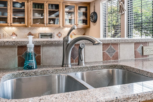 interior details with a sink, decorative backsplash, and glass insert cabinets