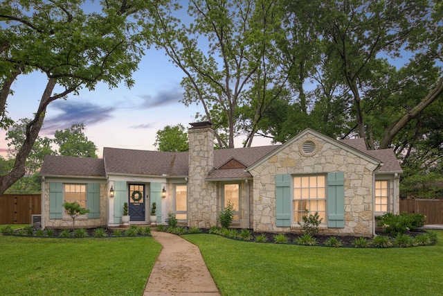 ranch-style home featuring a chimney, fence, a yard, and stone siding